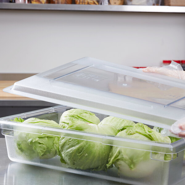 A person holding a Carlisle clear plastic food storage lid filled with lettuce.