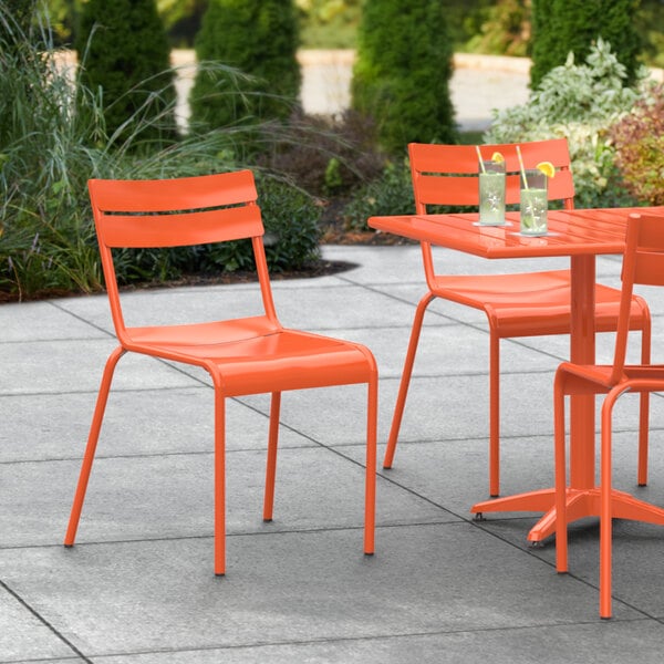 An orange Lancaster Table & Seating outdoor side chair on a patio with an orange table and chairs.
