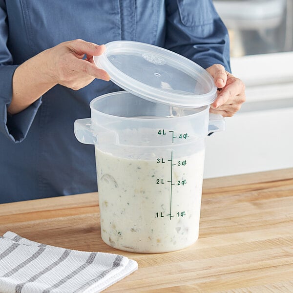 A woman pouring white liquid from a measuring cup into a plastic container with a lid.