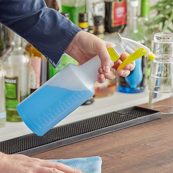 A hand holding a yellow Lavex spray bottle over a counter spraying blue liquid.