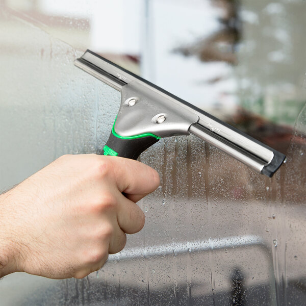 A hand holding a Unger ErgoTec window squeegee to clean a window.