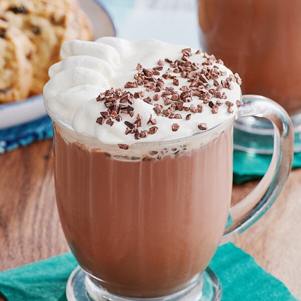 A glass mug of hot chocolate with whipped cream and chocolate chips.