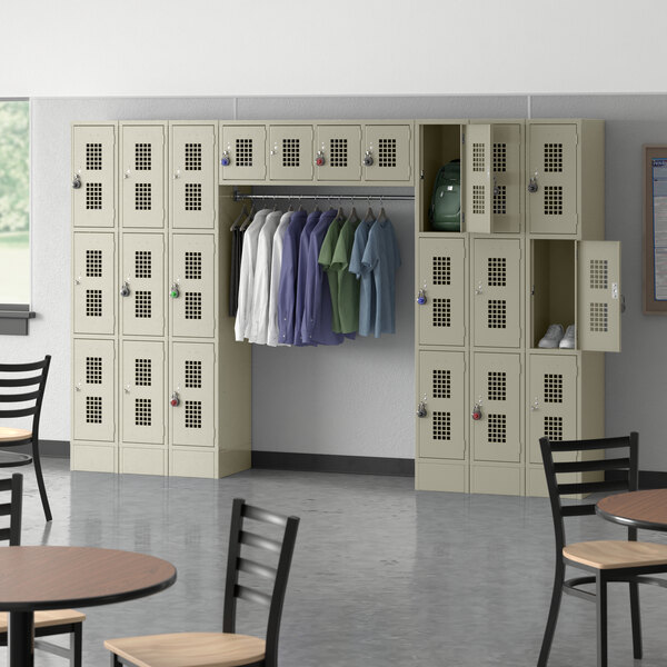 A room with a Regency beige locker with tables and chairs and a garment rack with shirts.