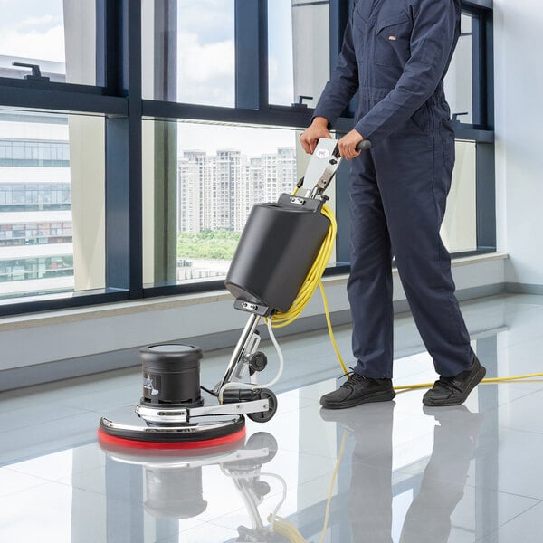 A man in a blue uniform using a Lavex Dual Speed Rotary Floor Machine to clean the floor.