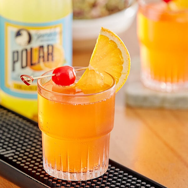 A glass of Polar orange drink with a slice of orange and a cherry on top.