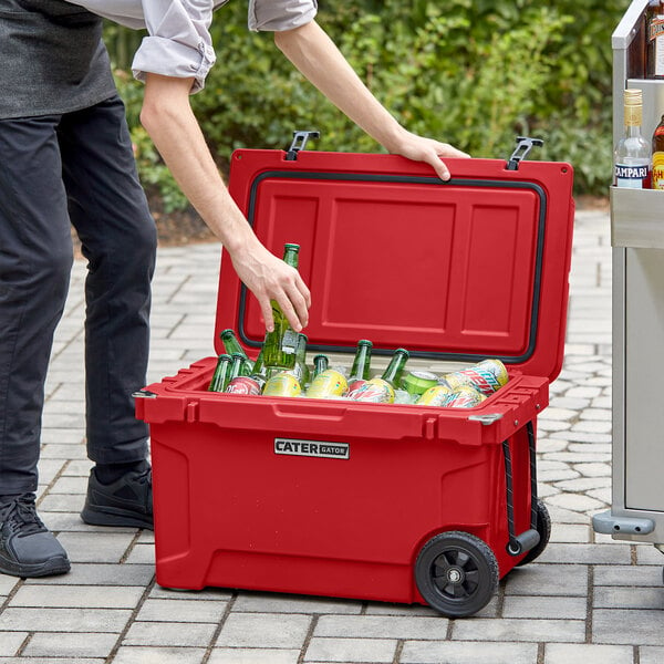 A person in black pants putting beer bottles in a red CaterGator outdoor cooler.