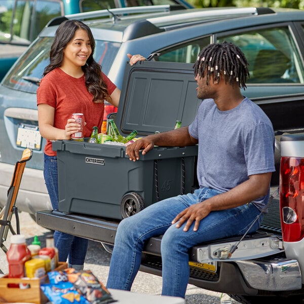 A man and woman sitting on the tailgate of a truck next to a CaterGator outdoor cooler.