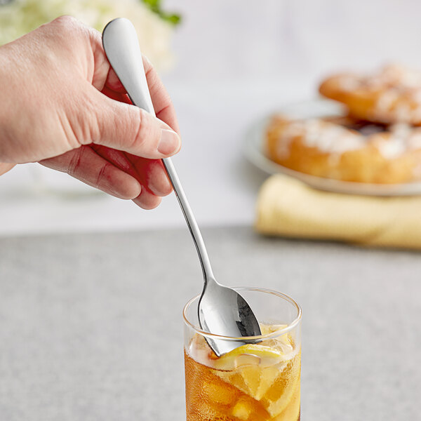 A hand holding an Acopa Vittoria stainless steel iced tea spoon in a glass of tea.