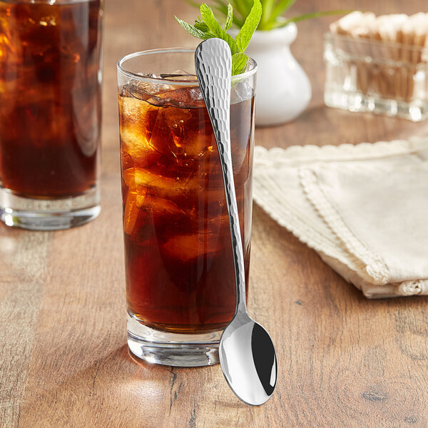 An Acopa stainless steel iced tea spoon in a glass of iced tea with a leaf.