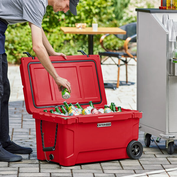 A man putting a can of beer into a red CaterGator outdoor cooler.