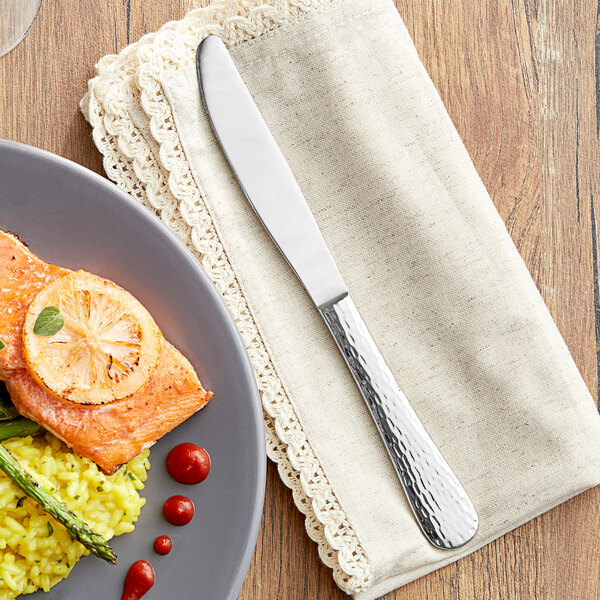 An Acopa Inspira stainless steel table knife on a napkin next to a plate of food with lemon slices and rice.