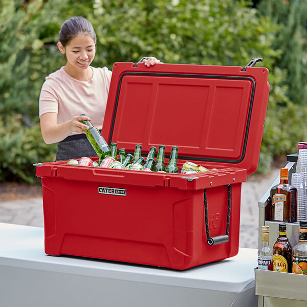 A woman putting red beer bottles in a red CaterGator outdoor cooler.
