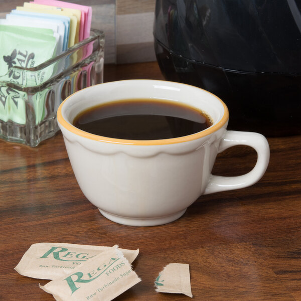 A CAC Seville ivory china cup of coffee on a table with sugar packets.