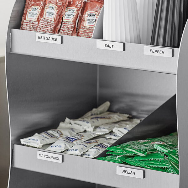 A stainless steel shelf with magnetic condiment labels holding various condiments.