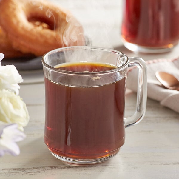 A glass mug of Crown Beverages Organic Donut Shop Whole Bean Coffee next to a cup of coffee and donuts.
