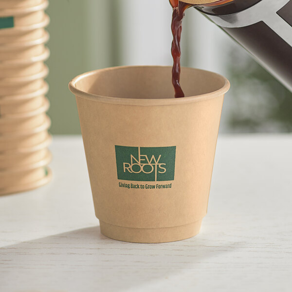 A close up of brown liquid being poured into a New Roots smooth double wall Kraft paper hot cup.