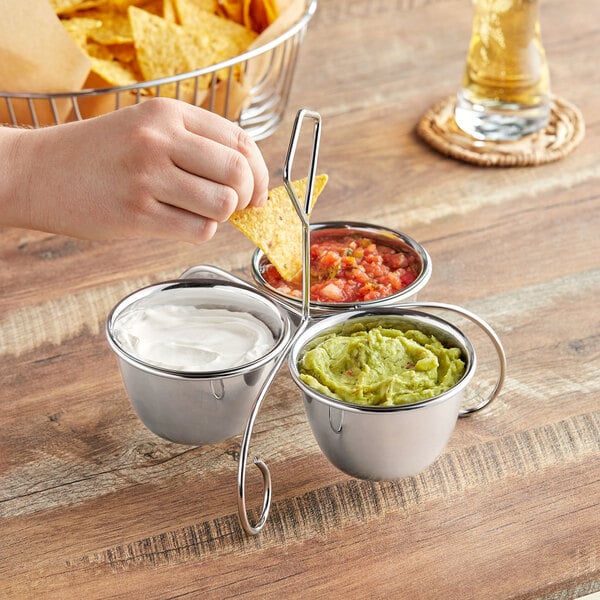 A person using a Choice stainless steel condiment server to dip a chip into guacamole.