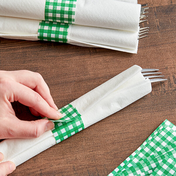 A person wrapping a napkin with green and white checkered paper.