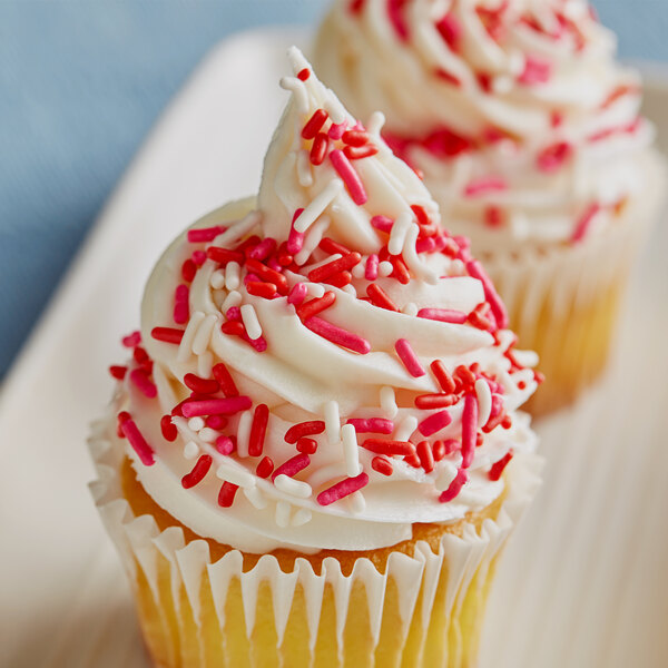 A cupcake with white frosting and Valentine's Day sprinkle mix on top.