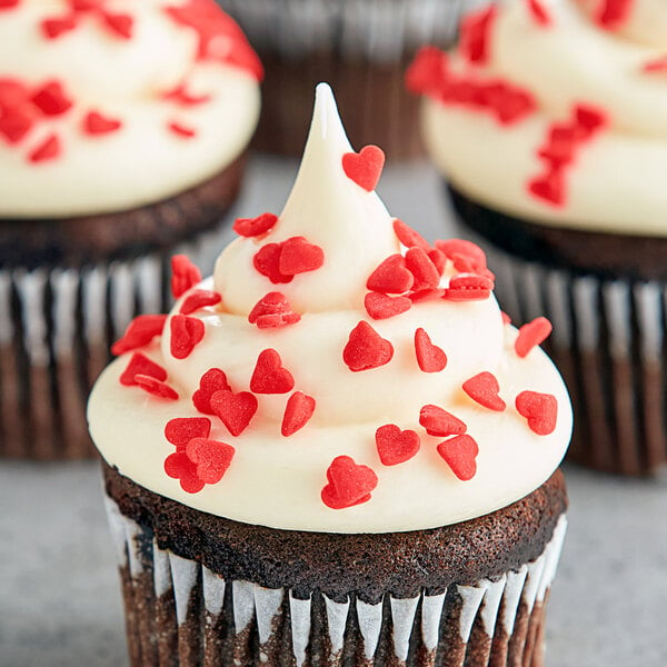 A chocolate cupcake with white frosting and Red Heart Sprinkles.