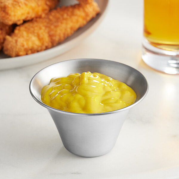 An American Metalcraft stainless steel sauce cup filled with yellow sauce next to fried chicken fingers.