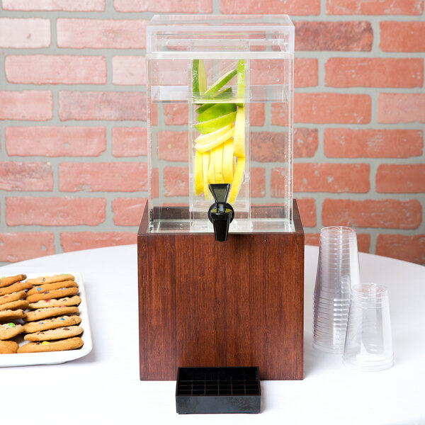 A Cal-Mil dark wood infusion beverage dispenser on a table with cookies and plastic cups.