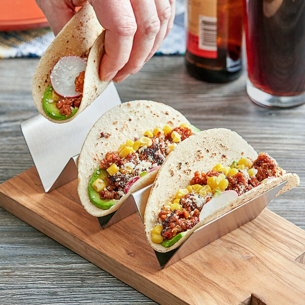 A person holding tacos in an American Metalcraft stainless steel taco holder.