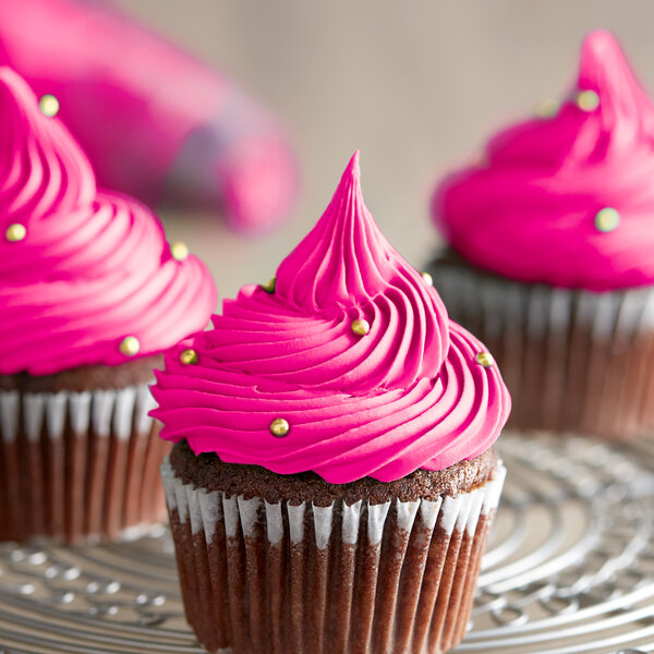 A close up of three cupcakes with pink frosting.