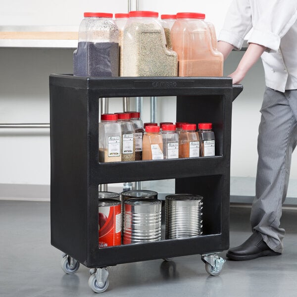 A man pushing a black Cambro service cart with food and spices on it.