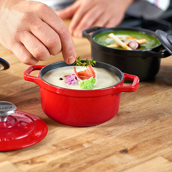 A person using a Chasseur ruby red enameled cast iron pot to prepare food.