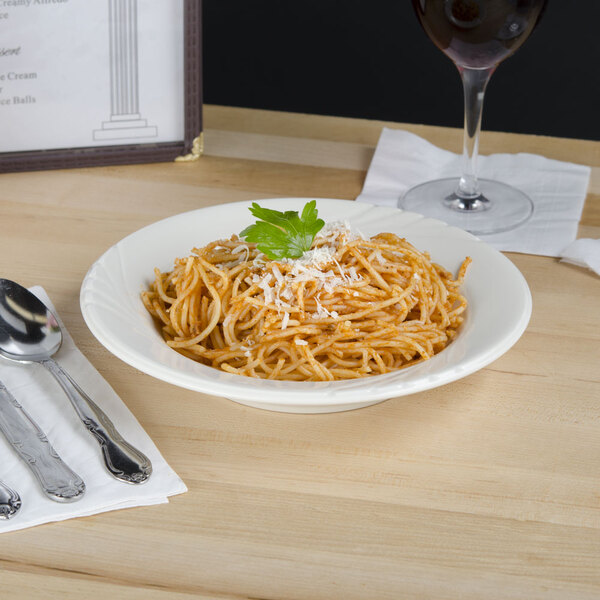 A Tuxton eggshell rim china bowl filled with spaghetti and a glass of wine on a table.