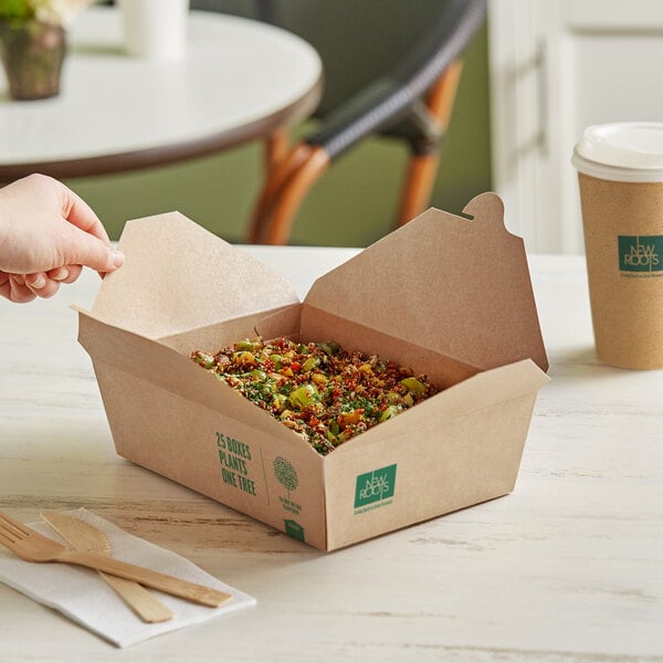 A hand holding a New Roots Kraft PLA-Lined take-out box of food on a table.