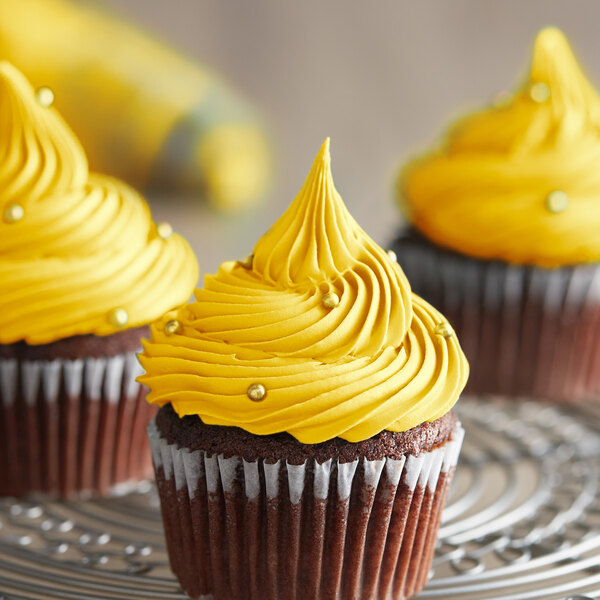 Three cupcakes with yellow frosting on a metal rack.