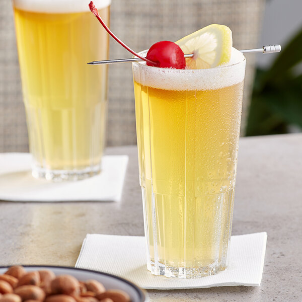 A pair of Duralex highball glasses filled with yellow liquid and cherries.