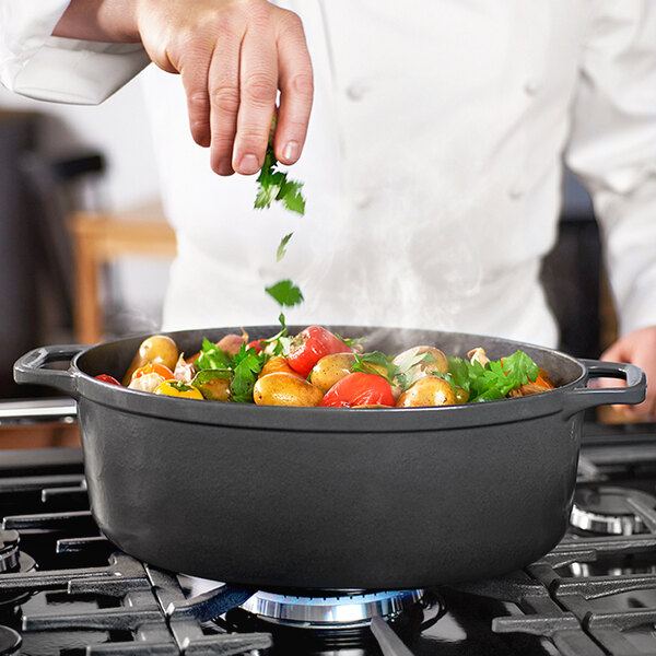 A person adding herbs to a Chasseur black enameled cast iron pot of vegetables and meat.