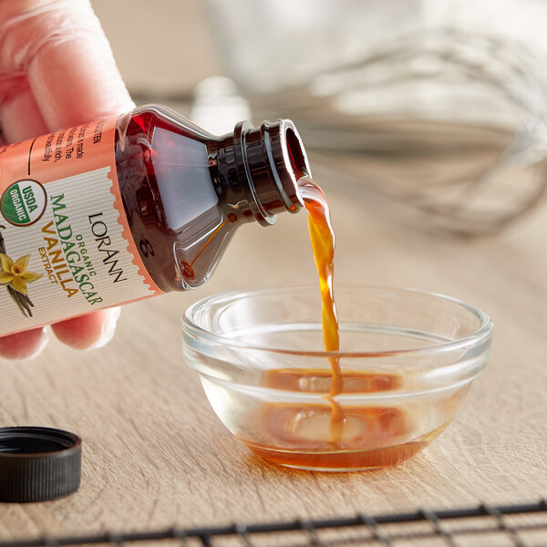A hand pours LorAnn Organic Madagascar Vanilla extract into a glass bowl.