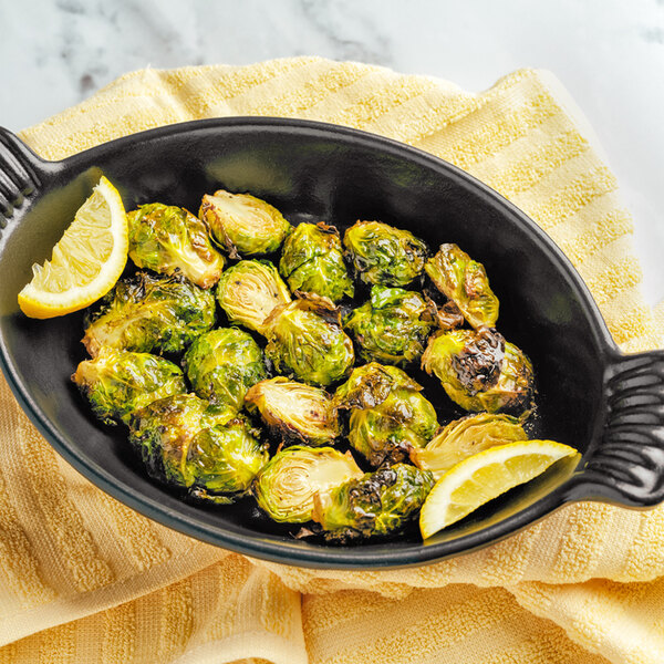 A black Chasseur enameled cast iron oval casserole dish with brussels sprouts and lemon wedges.