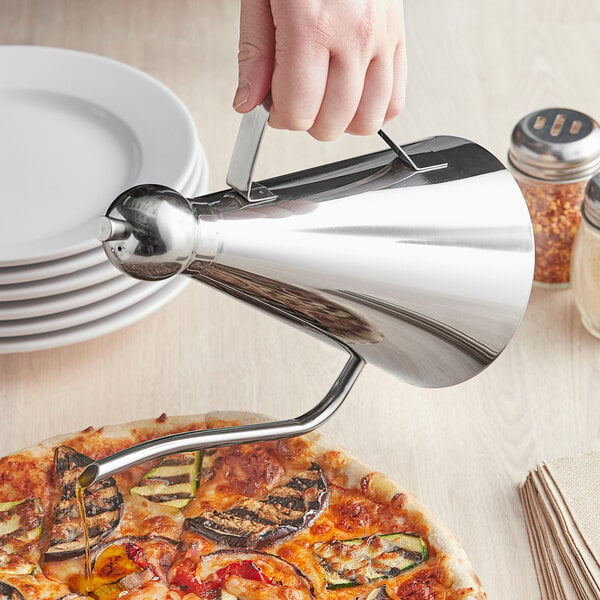 A hand using a GI Metal stainless steel oil dispenser to pour oil over a pizza.
