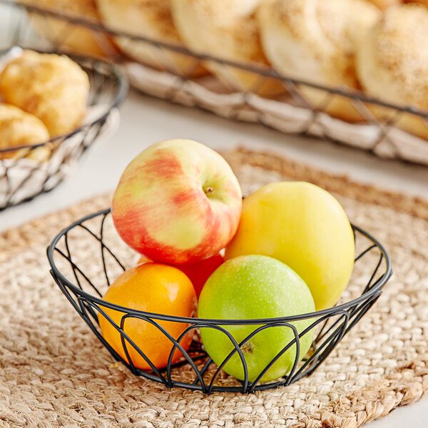 A black Tablecraft round wire basket filled with green and red apples.