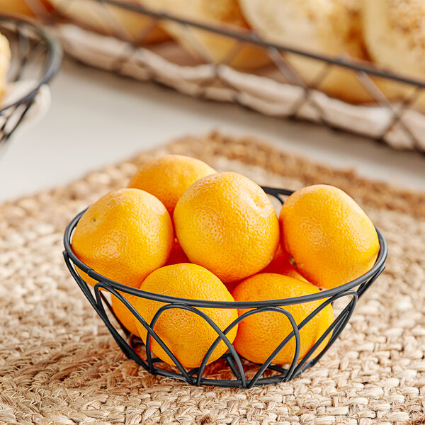 A Tablecraft round wire basket filled with oranges on a table.