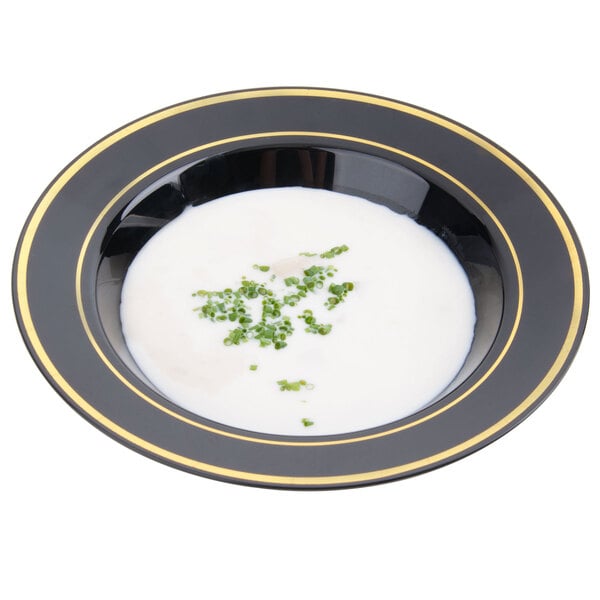 A Fineline black plastic soup bowl with gold bands filled with white soup and green onions.