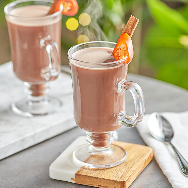 A glass cup of UPOURIA Mexican spice hot chocolate on a white surface.