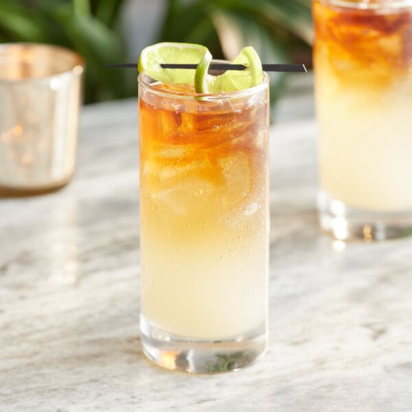 A glass of Goslings ginger beer with a straw and lime slices on top.