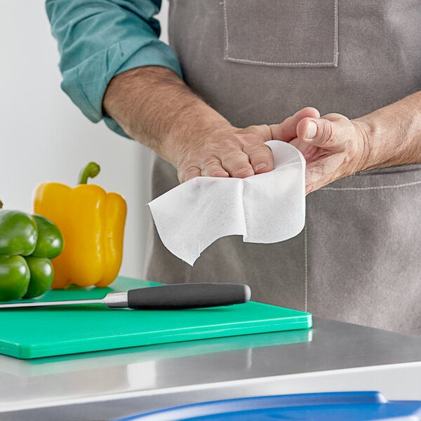 A man using WipesPlus Lemon Scent hand sanitizing wipes to clean a cutting board.