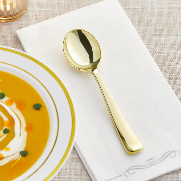 A Visions gold plastic soup spoon on a napkin next to a bowl of soup.