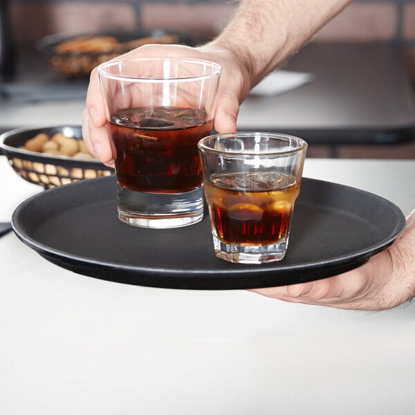 A person holding a Carlisle non-skid serving tray with two glasses of brown liquid.