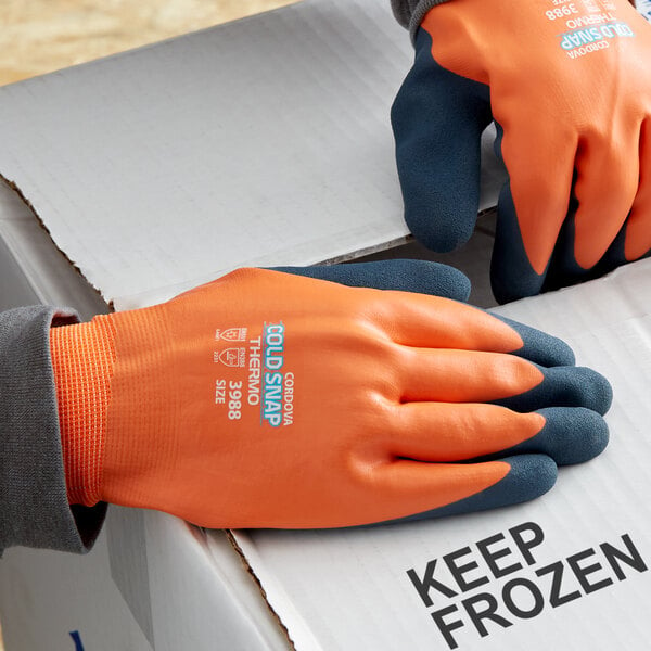 A pair of small orange and blue Cordova Cold Snap Thermo gloves on a hand.