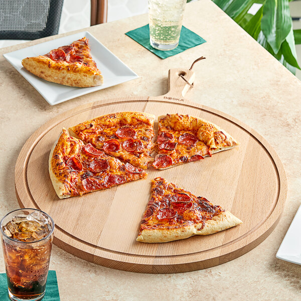 A pepperoni pizza on a Boska round beech wood serving board with a slice cut out.
