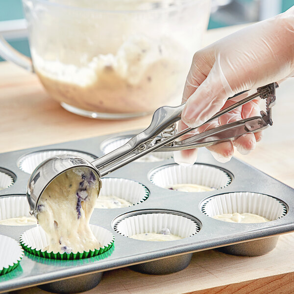 A person using a Choice #16 stainless steel scoop to fill a cupcake tin.