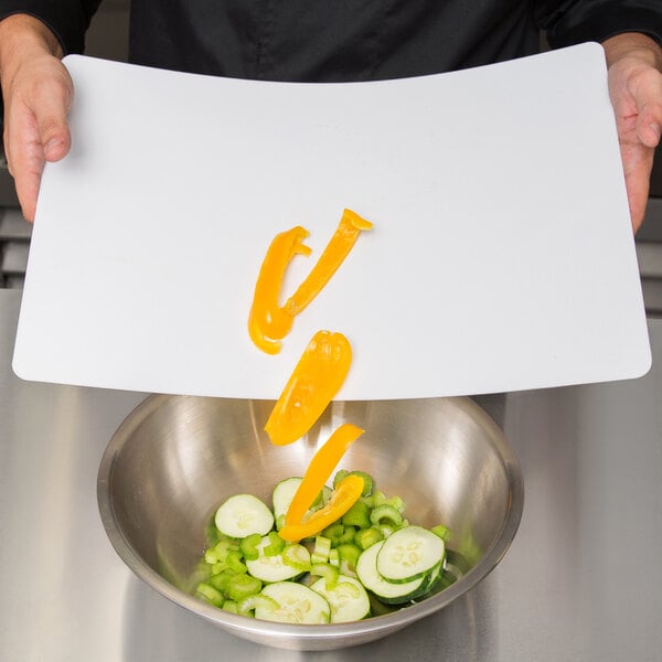 A person holding a Tablecraft white flexible cutting board over a bowl of vegetables.
